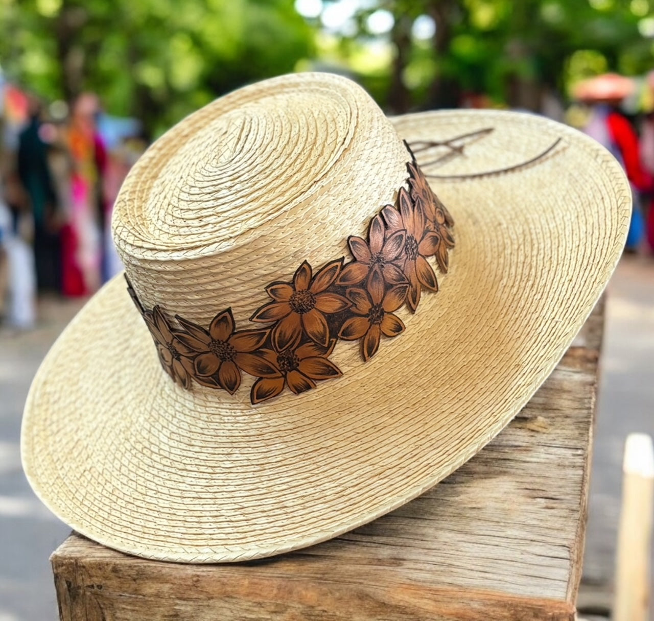 A straw hat with a hand-burned leather hat band featuring a floral design.