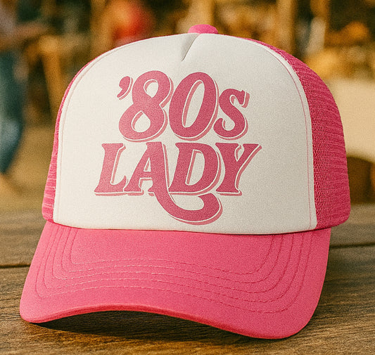 Pink and white cap with '80s Lady' text on a wooden surface
